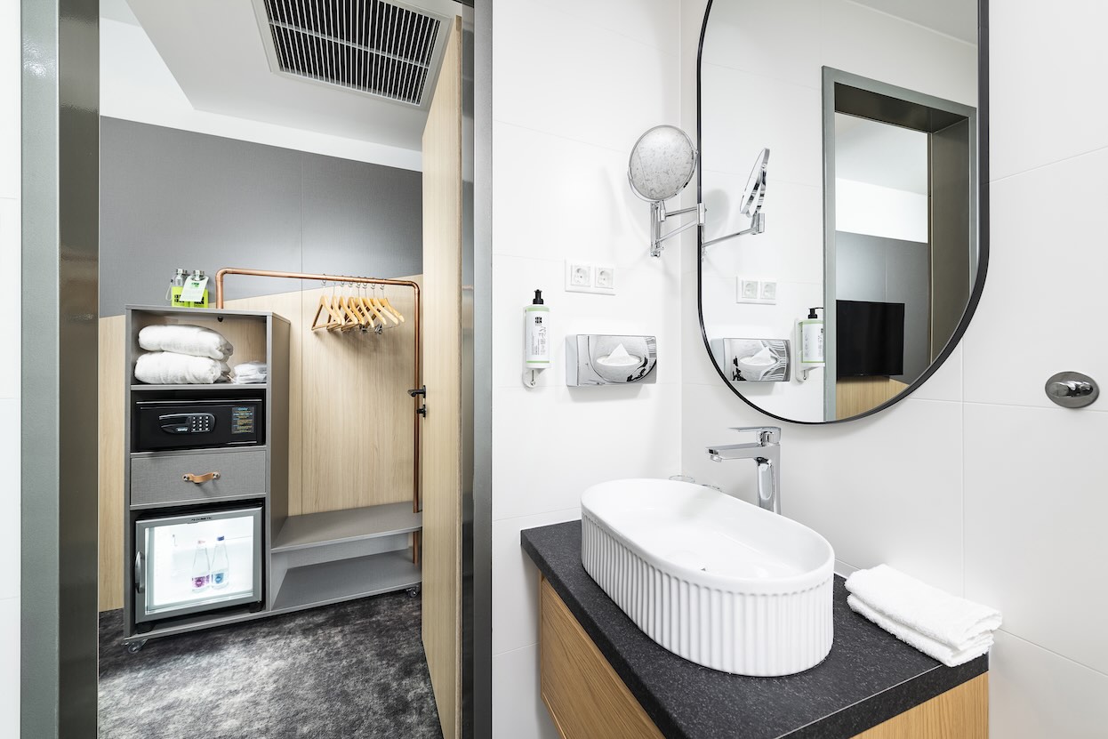 Nyitott előszobai szekrény széffel és minibárral, kilátással a fürdőszobai mosdóra.