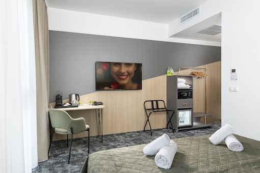 A szoba belső tere az ágy végével, íróasztallal és nyitott gardróbbal, benne széffel.