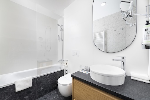 Modern fürdőszoba káddal, üveg zuhanyfallal, ovális mosdókagylóval és nagy tükörrel.